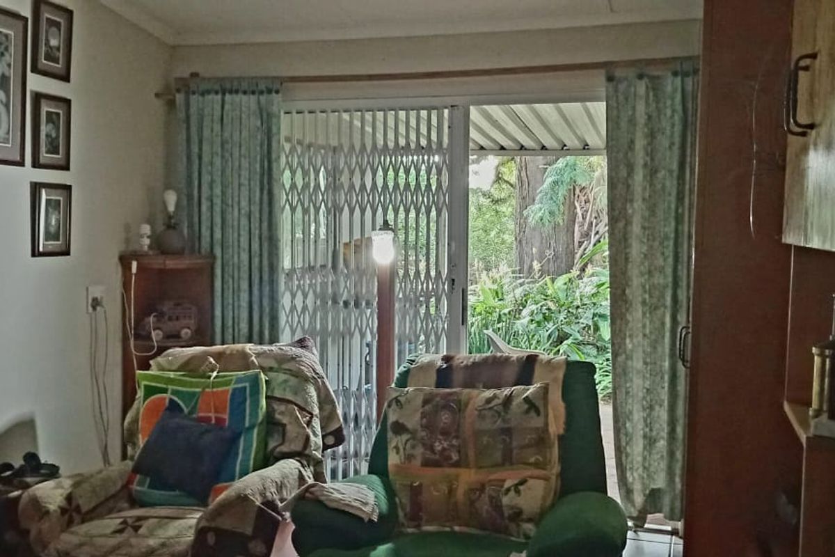 A living room featuring sliding glass doors with security gates, providing direct access to an outdoor garden area.