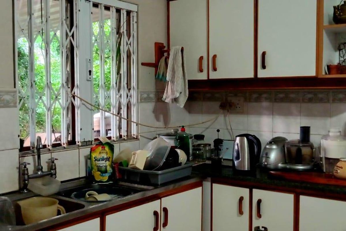 A functional kitchen featuring white cabinetry with wood trim, a double basin sink, and a tiled backsplash with security bars on the windows.