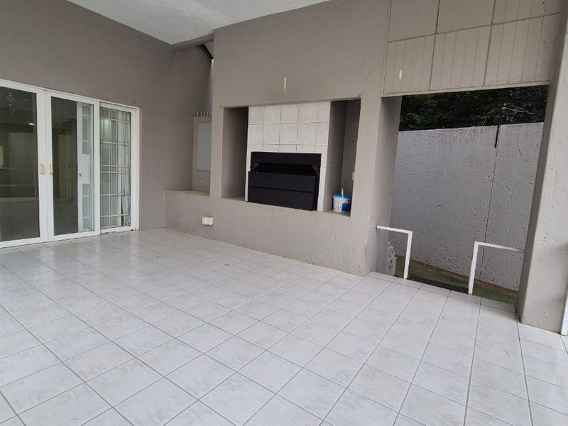 Covered patio area featuring a built-in braai, tiled flooring, and direct access to the interior through sliding glass doors.