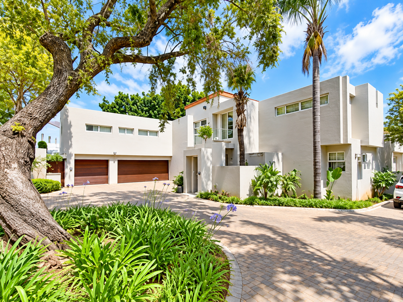 Modern double-story cluster home featuring a paved driveway, double garage, and well-maintained landscaped garden with mature trees.