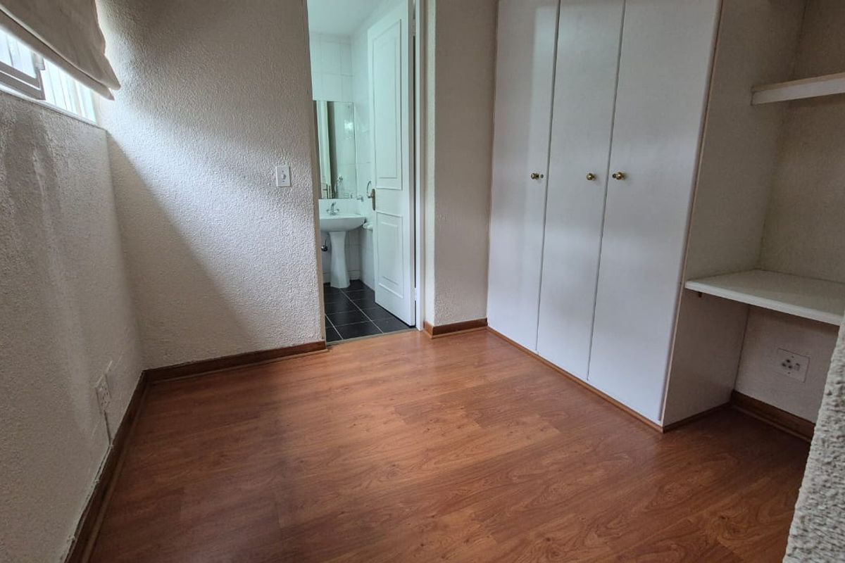 A vacant bedroom featuring laminate flooring, built-in cupboards, and direct access to an en-suite bathroom with a pedestal basin.