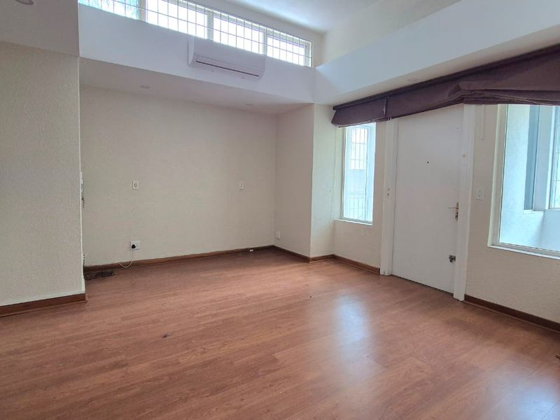 An empty living room featuring laminate flooring, a split-system air conditioner, and high clerestory windows providing natural light.