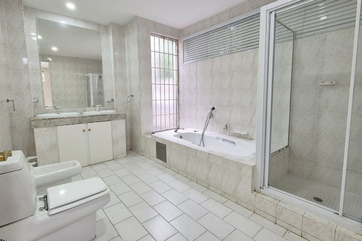 Spacious bathroom featuring a double vanity, built-in bathtub, separate shower enclosure, and bidet, finished with neutral wall and floor tiling.