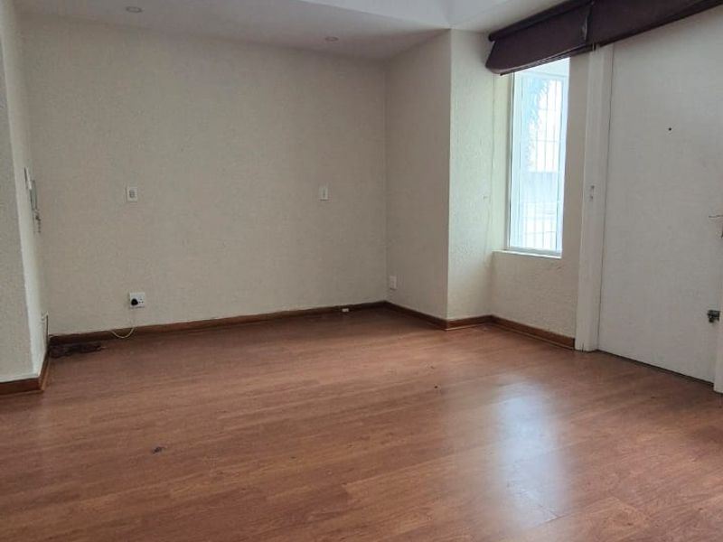 An empty living room featuring laminate flooring, a split-system air conditioner, and high clerestory windows providing natural light.