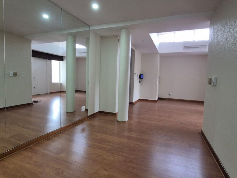Spacious, empty living area featuring laminate flooring, structural columns, a large wall mirror, and a skylight providing natural light.