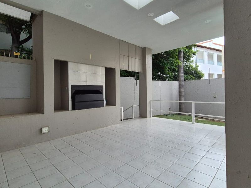Covered patio area featuring a built-in braai, tiled flooring, and skylights, overlooking a private garden space.