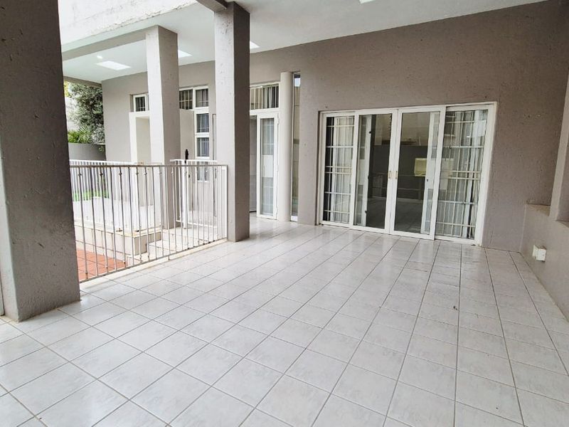 Spacious covered patio featuring tiled flooring, a built-in braai, and direct access to the pool area through sliding glass doors.