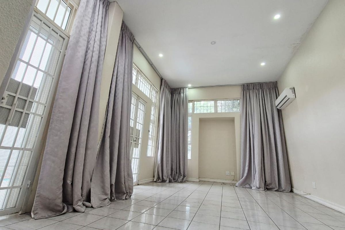 Spacious, light-filled living area featuring tiled flooring, recessed lighting, a wall-mounted air conditioning unit, and large glass doors providing access to the exterior.
