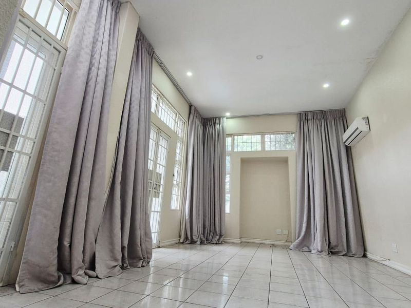 Spacious, light-filled living area featuring tiled flooring, recessed lighting, a wall-mounted air conditioning unit, and large glass doors providing access to the exterior.