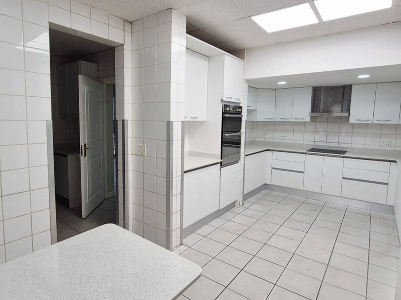 A spacious, functional kitchen featuring white built-in cabinetry, stone countertops, integrated oven, and hob, with tiled walls and flooring throughout.