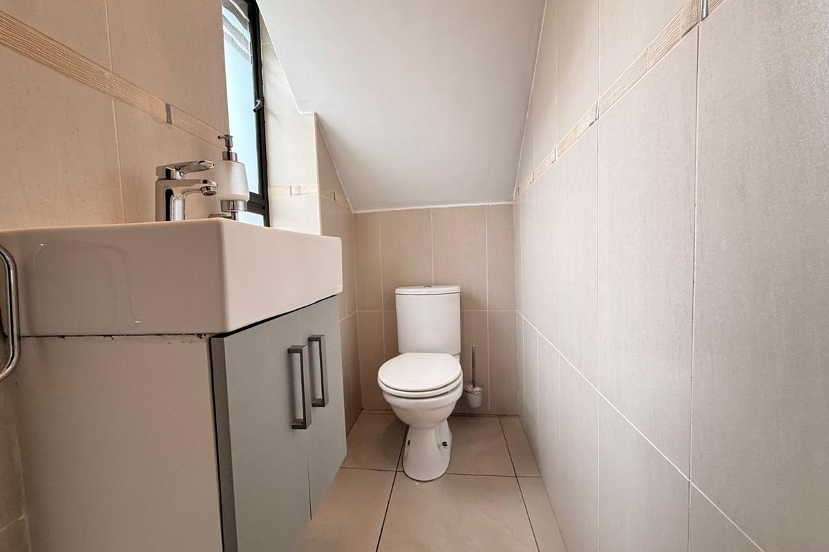 A compact guest bathroom featuring a modern wall-mounted vanity with basin and a standard toilet, finished with neutral floor-to-ceiling wall tiles.
