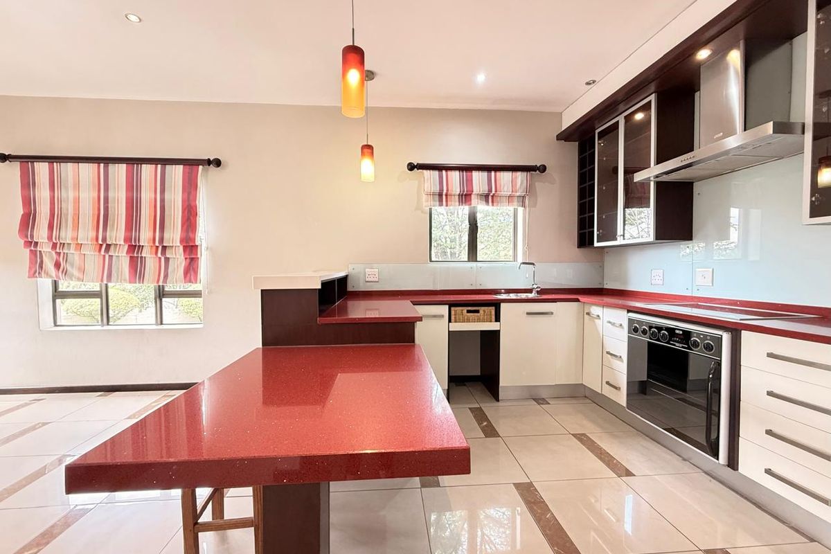 Modern kitchen featuring a breakfast bar, red stone countertops, built-in oven, extractor fan, and tiled flooring with decorative inlays.