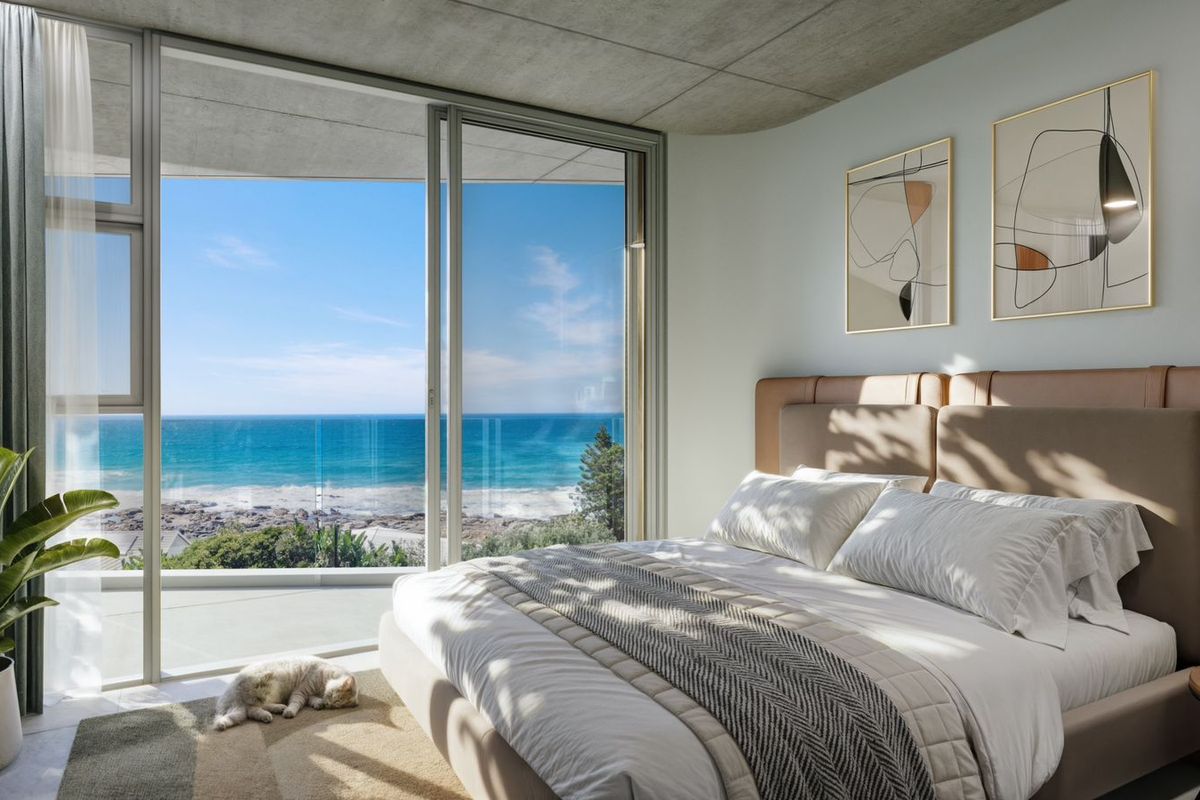 Modern bedroom featuring floor-to-ceiling sliding glass doors that open to a private balcony with expansive ocean views and a raw concrete ceiling.