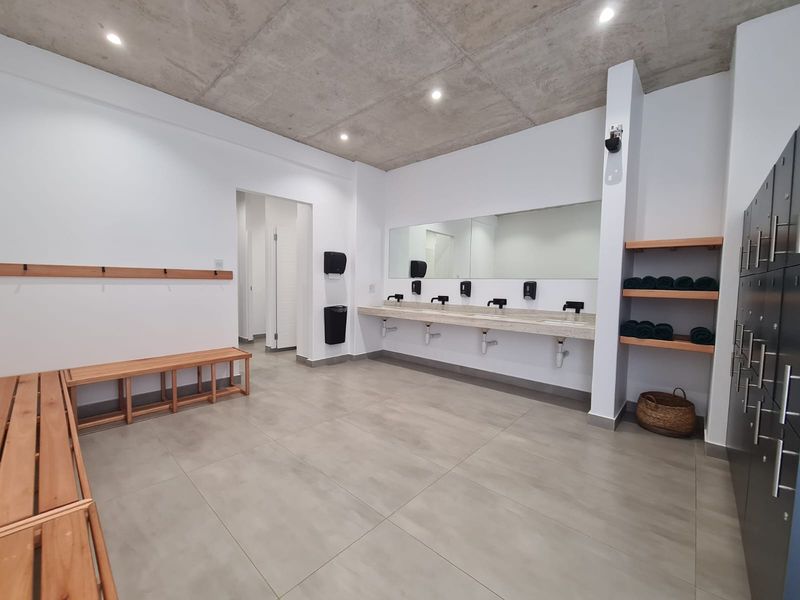 Modern communal bathroom or changing area featuring a concrete ceiling, tiled flooring, multiple vanity basins, and built-in storage lockers.