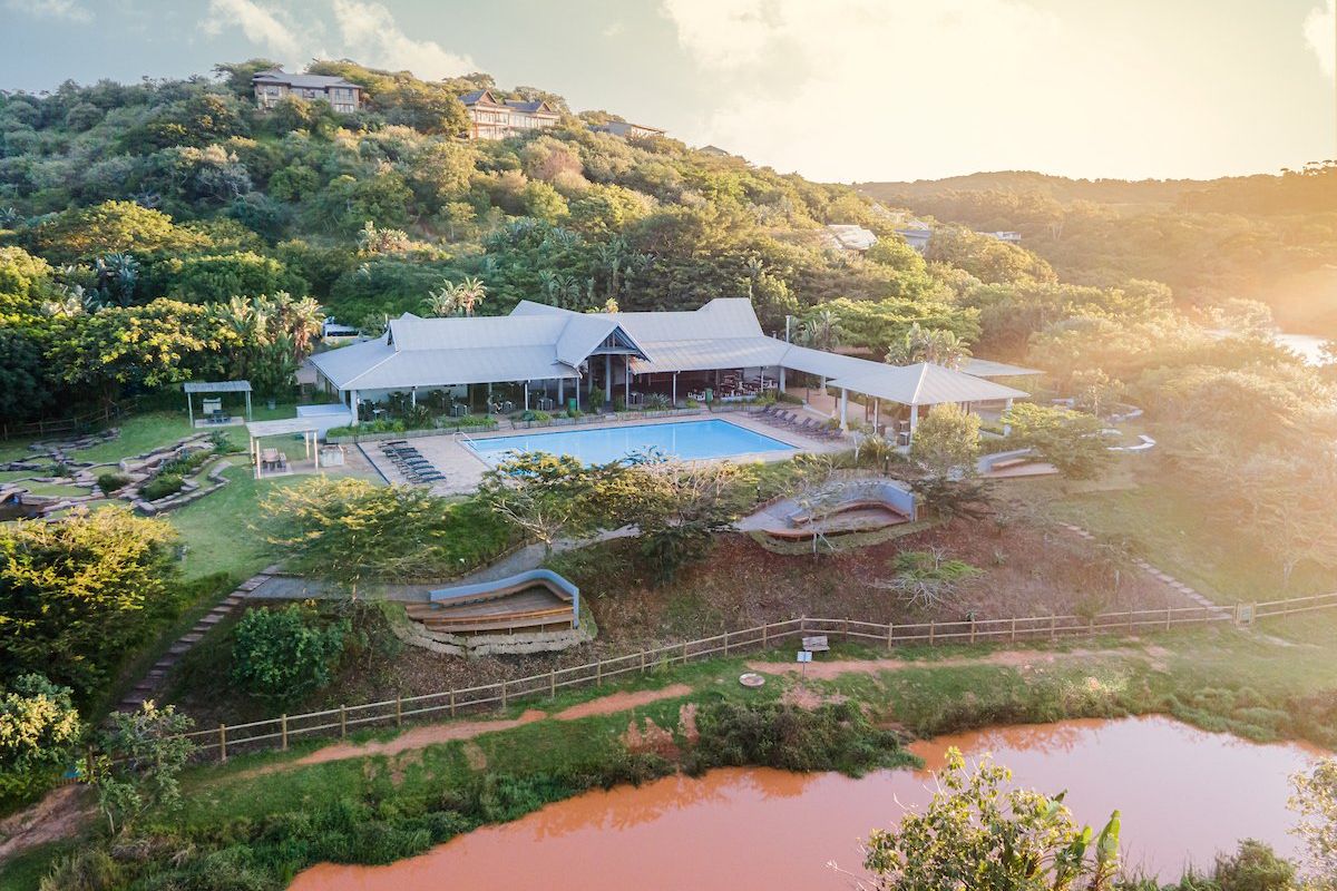 Aerial view of a residential clubhouse facility featuring a swimming pool, landscaped grounds, and surrounding natural hillside terrain.