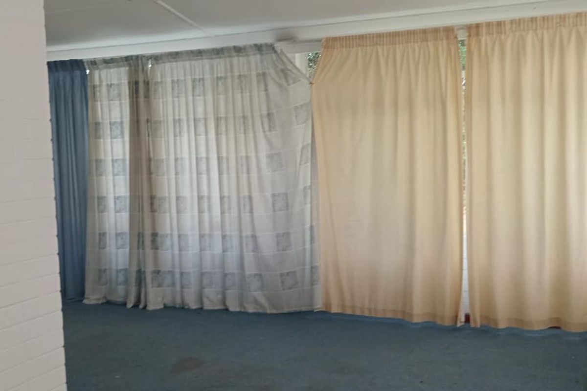 An interior living space featuring painted brick walls and large windows covered by curtains, with carpeted flooring throughout.