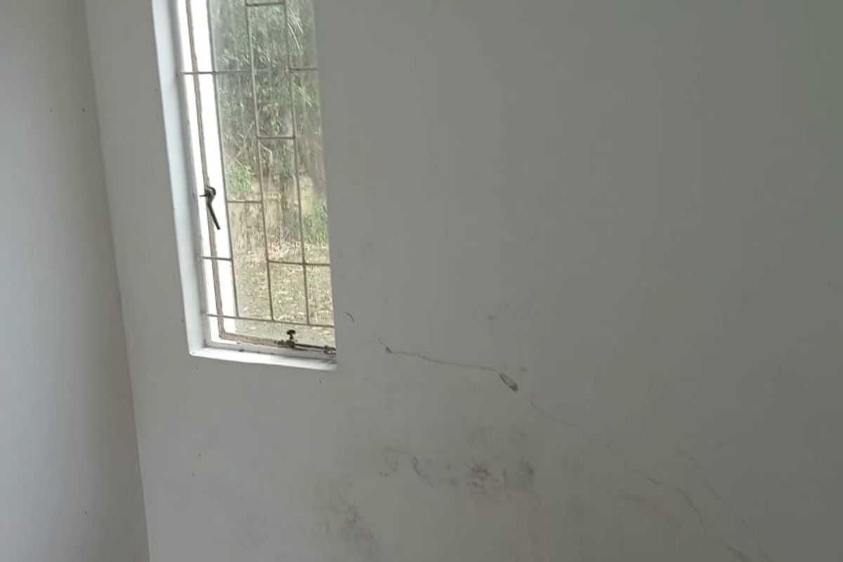 A view of an interior wall featuring a window with security bars and a visible structural crack in the plaster.