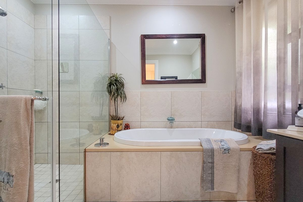 A well-maintained bathroom featuring a built-in bathtub, a glass-enclosed walk-in shower, and a vanity basin with neutral wall tiling.