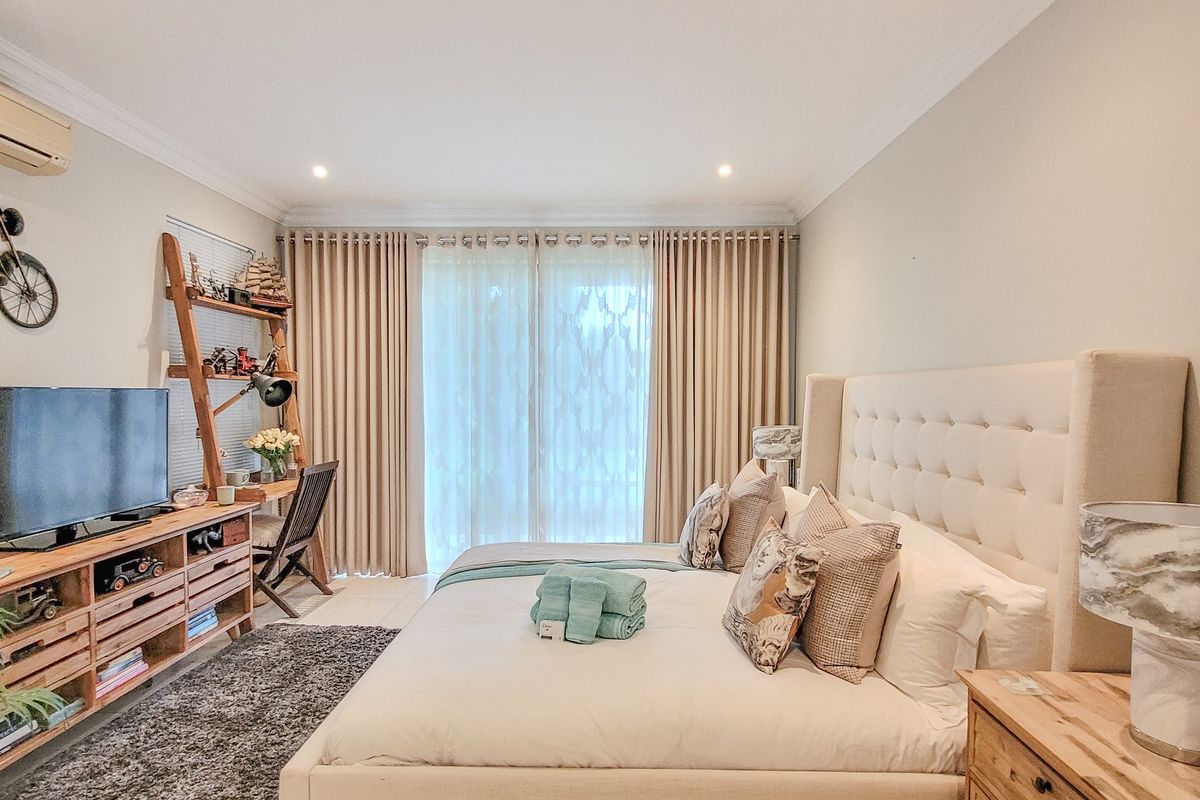 A well-maintained bedroom featuring neutral tones, crown molding, tiled flooring, and a wall-mounted air conditioning unit with access to a private balcony.