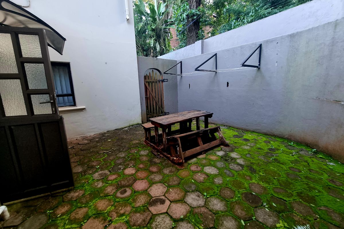 A private rear courtyard featuring paved flooring with significant moss growth, a boundary wall with mounted drying racks, and a small wooden gate.