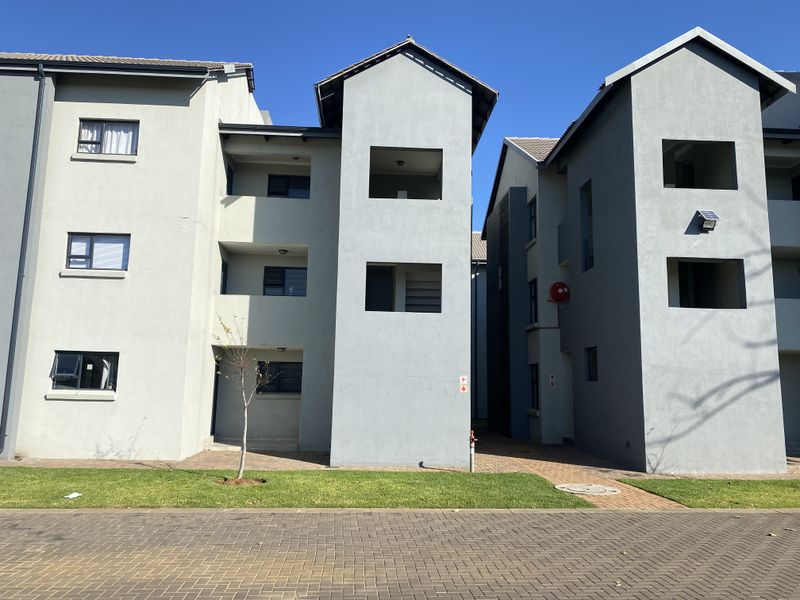 Exterior view of a modern townhouse complex featuring multi-story grey facades, paved walkways, and manicured lawn areas.