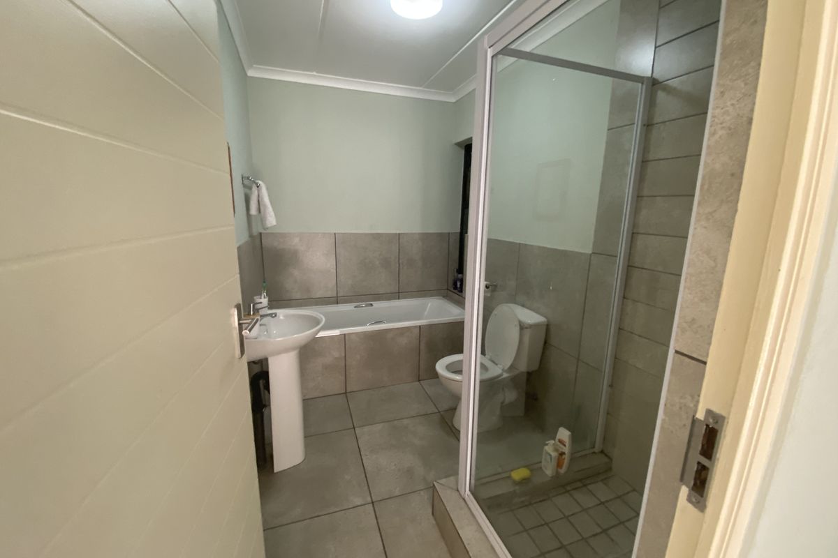 A functional bathroom featuring a pedestal basin, a built-in bathtub, and a separate glass-enclosed shower with neutral floor and wall tiling.