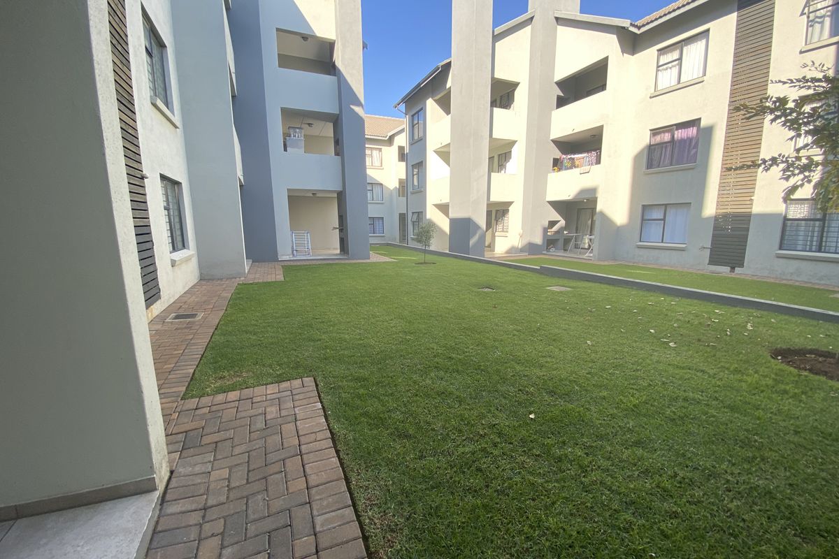 A view of the communal garden area between townhouse blocks, featuring paved walkways, manicured lawn, and multi-story residential building facades.