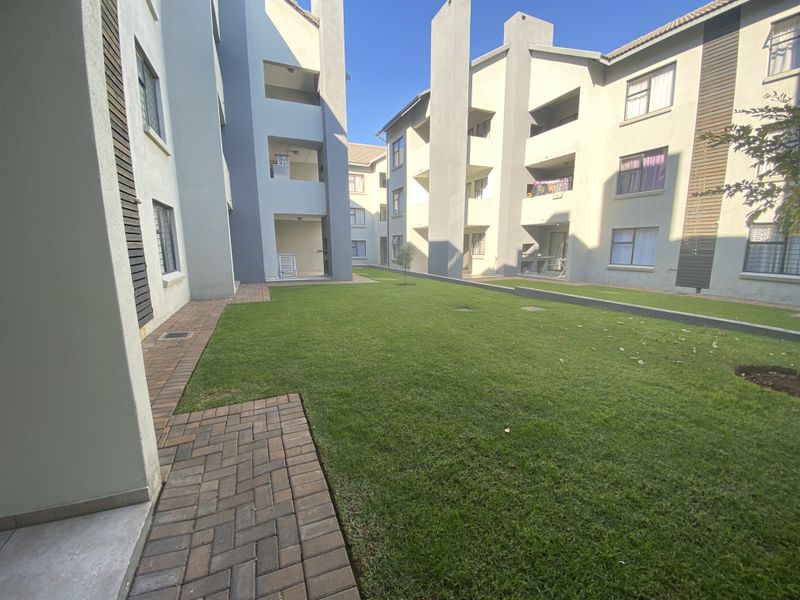 A view of the communal garden area between townhouse blocks, featuring paved walkways, manicured lawn, and multi-story residential building facades.