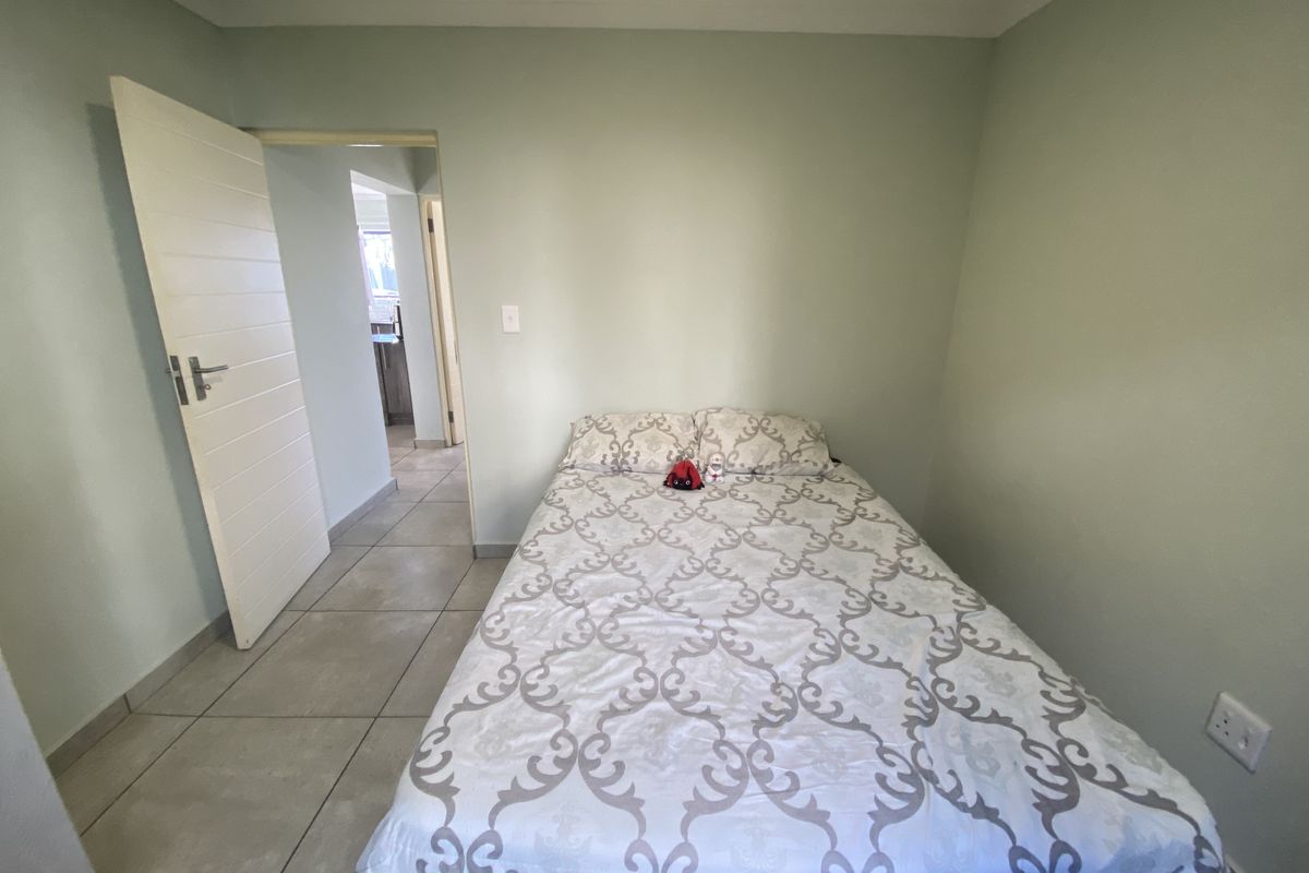 A bedroom featuring tiled flooring and neutral wall paint, with a doorway leading to an adjacent hallway.