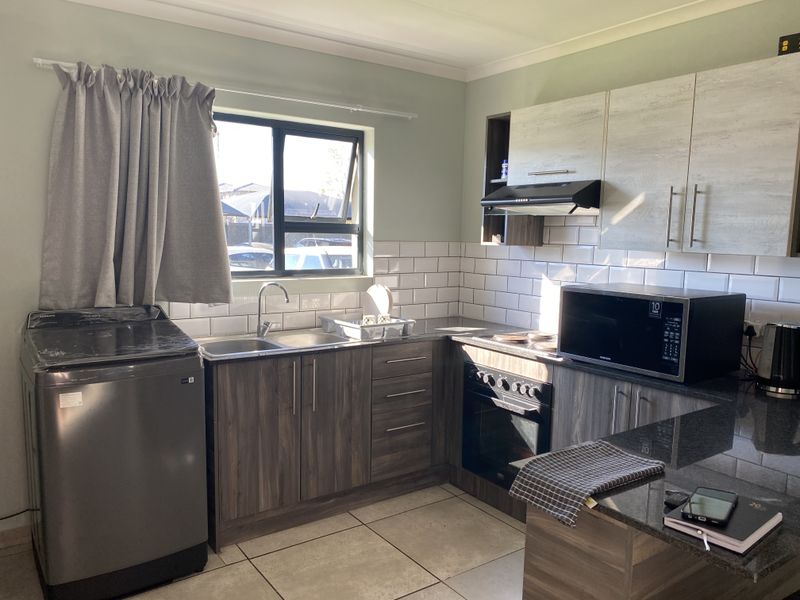 Modern kitchen featuring wood-grain cabinetry, granite countertops, subway tile backsplash, built-in oven, extractor fan, and a dedicated space for laundry appliances.