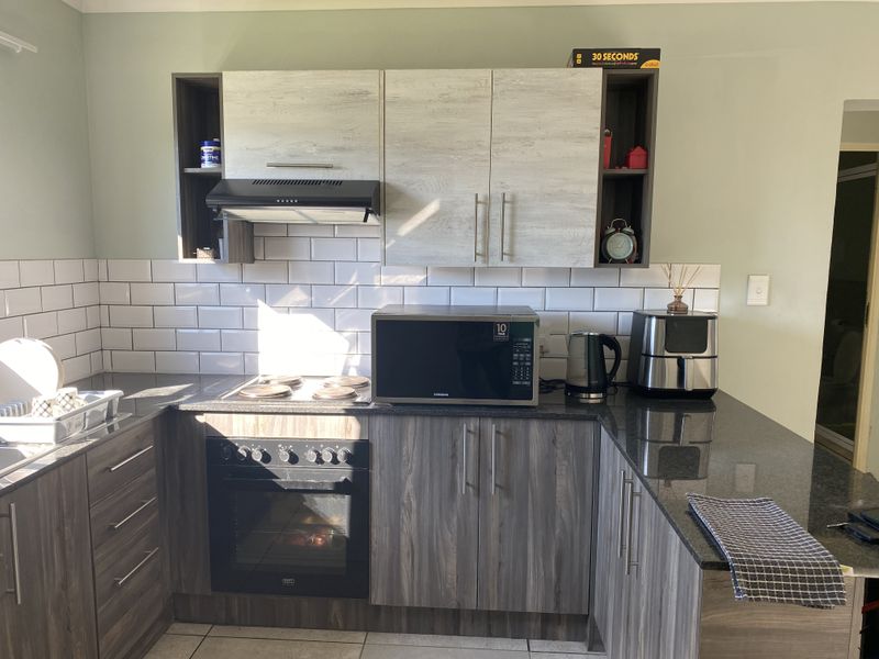 A modern kitchen featuring dark wood-grain lower cabinetry, light wood-grain upper cabinets, granite countertops, and a classic white subway tile backsplash.