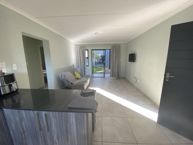 Open plan living area featuring tiled flooring, modern kitchen cabinetry with granite countertops, and sliding glass doors leading to a private garden.