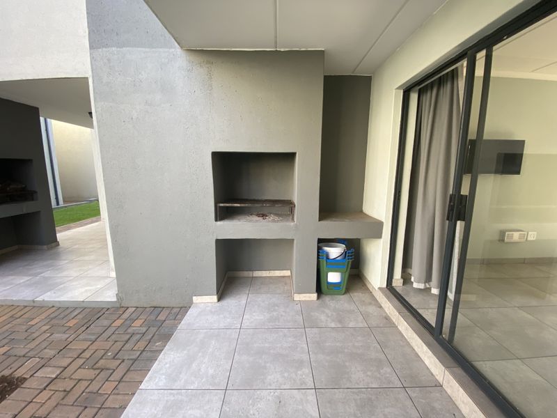 Covered patio area featuring a built-in braai, tiled flooring, and sliding glass door access to the interior living space.