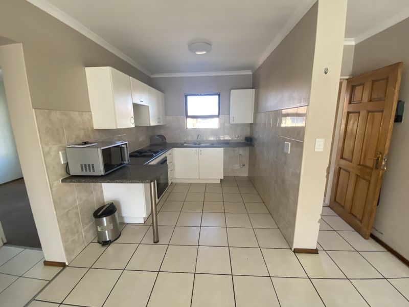 Functional kitchen featuring tiled flooring, built-in cabinetry, a tiled backsplash, and integrated oven and hob, offering a practical layout for daily use.