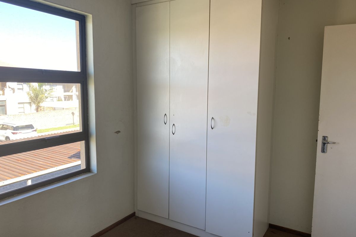 An empty bedroom featuring a built-in wardrobe, carpeted flooring, and a window with views of the surrounding complex.