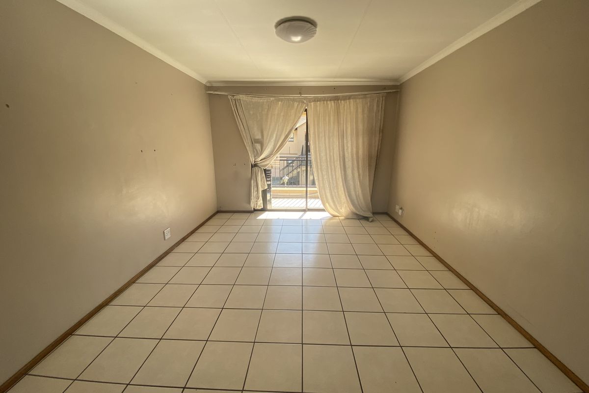 An empty living room featuring tiled flooring and a sliding glass door leading to a balcony, providing natural light and access to outdoor space.