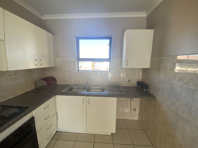 Functional kitchen featuring white cabinetry, laminate countertops, a double stainless steel sink, and tiled splashbacks with integrated oven and hob.