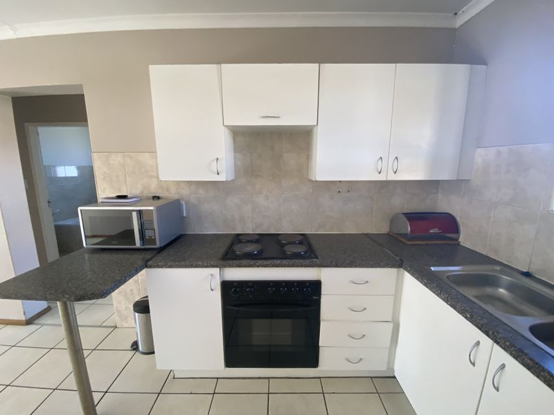 A functional kitchen featuring white cabinetry, dark laminate countertops, an integrated electric oven and hob, and tiled flooring.
