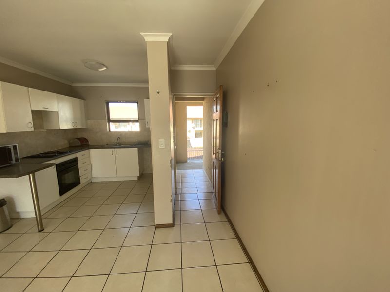 A functional kitchen area featuring tiled flooring, built-in cabinetry, and integrated oven and hob, leading to an adjacent hallway and exterior access.