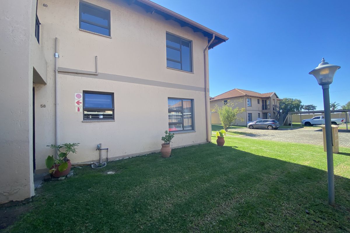 Rear view of the apartment building showing the plastered facade, aluminium window frames, and surrounding communal lawn area.