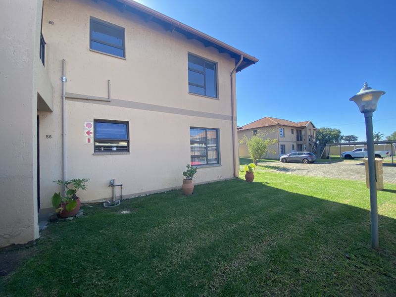 Rear view of the apartment building showing the plastered facade, aluminium window frames, and surrounding communal lawn area.
