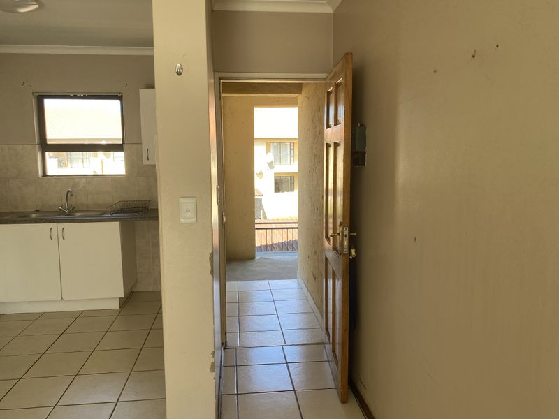 An open-plan kitchen area featuring tiled flooring and built-in cabinetry, with a doorway leading to an exterior balcony space.