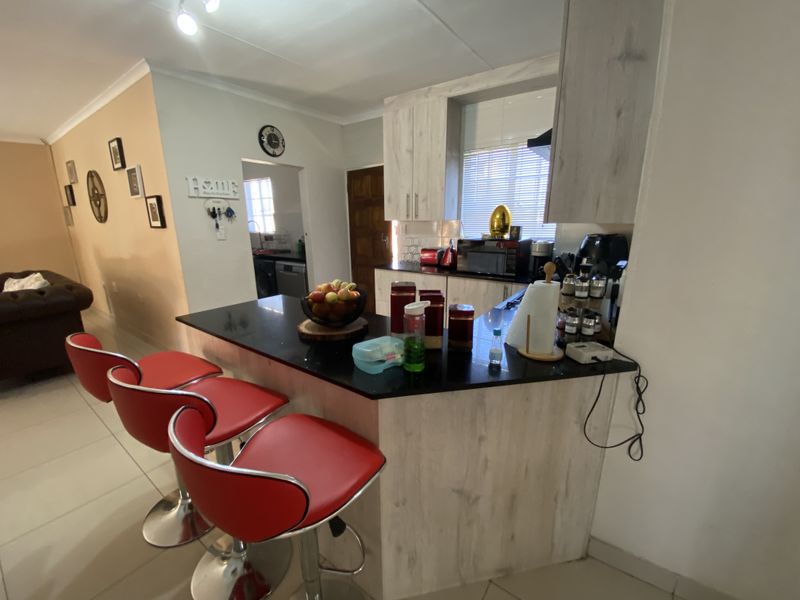 Open plan kitchen area featuring light wood-look cabinetry, a black granite breakfast bar, and tiled flooring, seamlessly connecting to the adjacent living space.