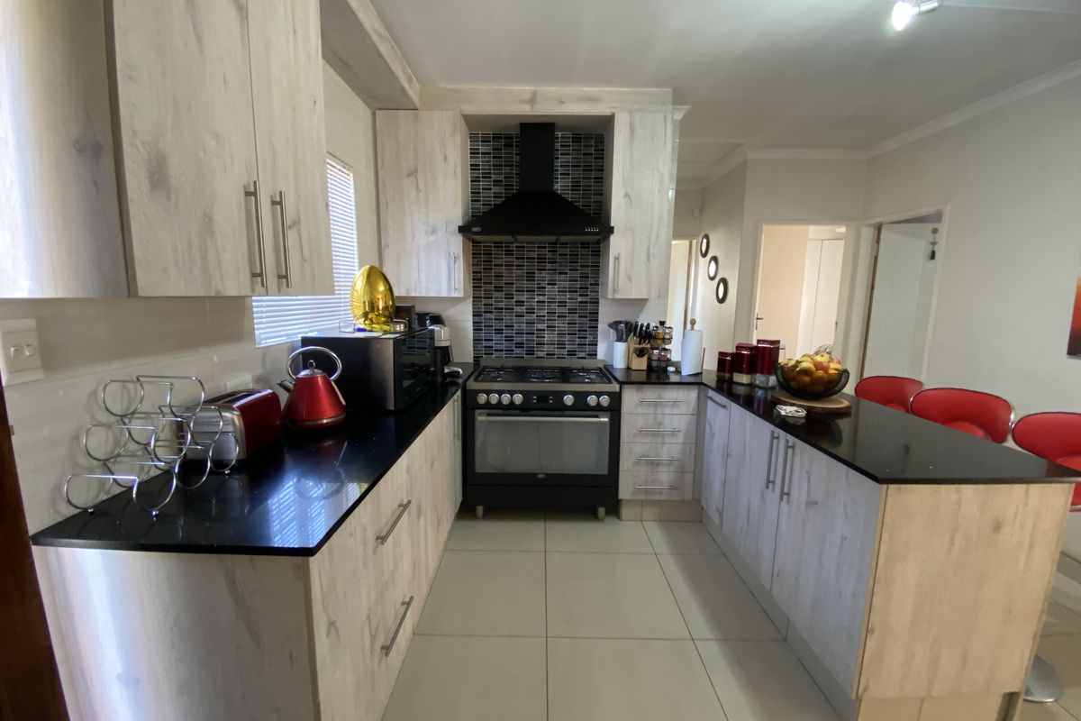 Modern kitchen featuring light wood-grain cabinetry, black granite countertops, a gas hob with extractor fan, and a convenient breakfast nook.