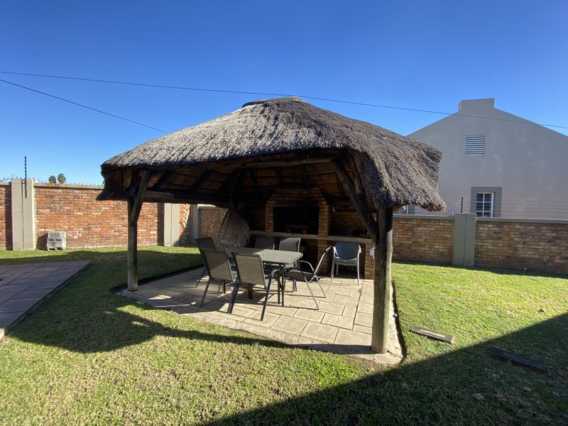 Outdoor entertainment area featuring a thatched lapa with a built-in brick braai, set on a paved patio within a private garden.