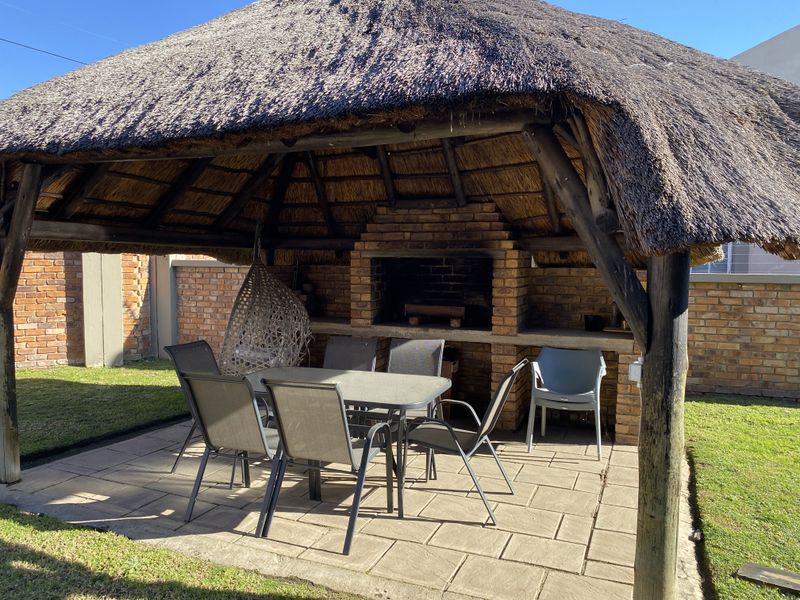 Outdoor entertainment area featuring a traditional thatched lapa with a built-in brick braai and paved flooring, set within a private garden space.