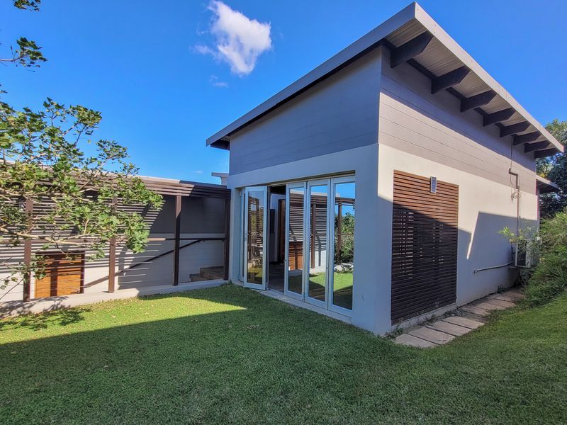 A modern rear exterior view featuring a structure with bi-fold glass doors, timber slat detailing, and an exposed rafter roof set within a landscaped garden.