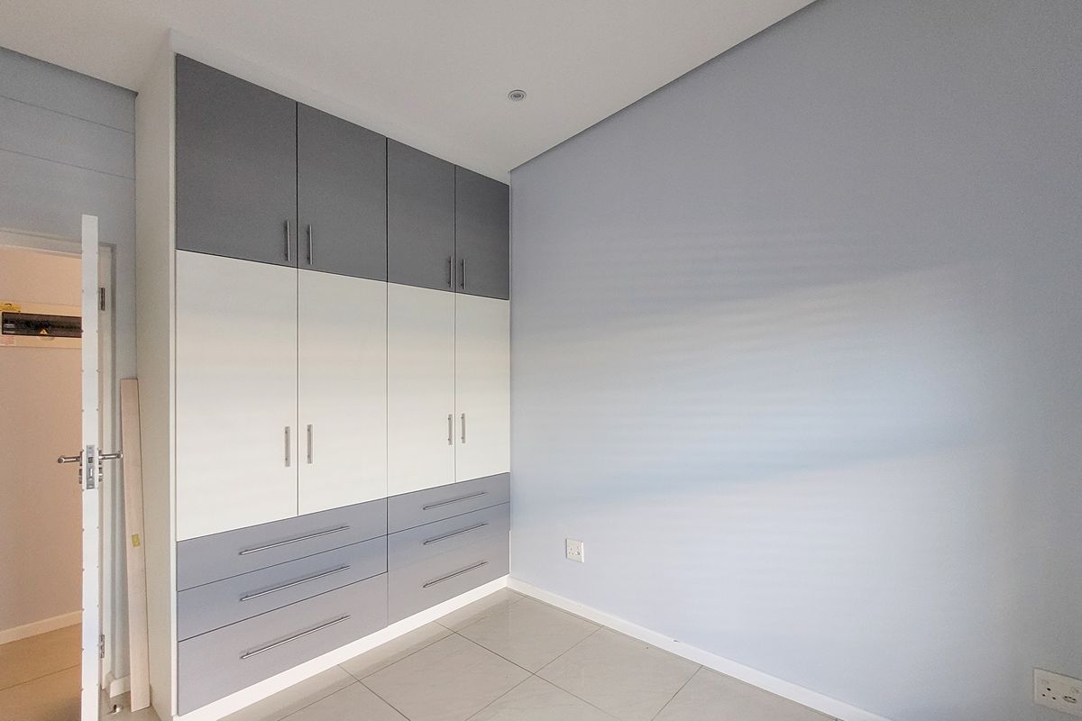 A clean, empty bedroom featuring modern two-tone built-in cupboards, neutral tiled flooring, and recessed lighting.