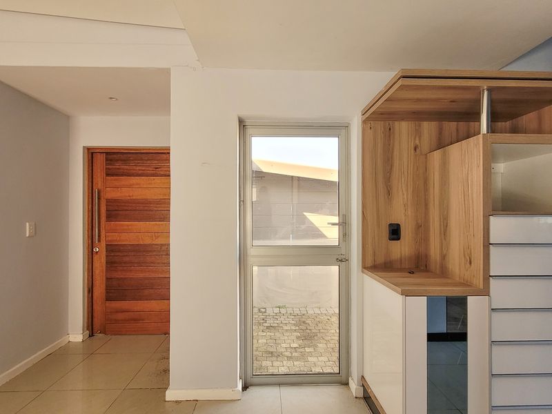 An entrance area featuring a solid timber front door, tiled flooring, and modern built-in cabinetry with a glass-panelled door leading to the exterior.