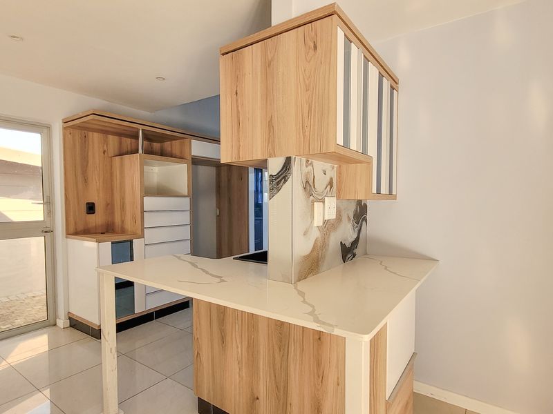 Modern kitchen featuring light wood cabinetry, stone countertops with marble-effect splashback, and tiled flooring, offering a clean and contemporary aesthetic.